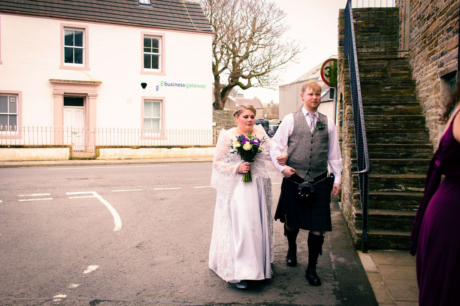 Bride in white dress and friend in traditional Scottish kilt walking together on a street after their wedding ceremony at the storehouse.