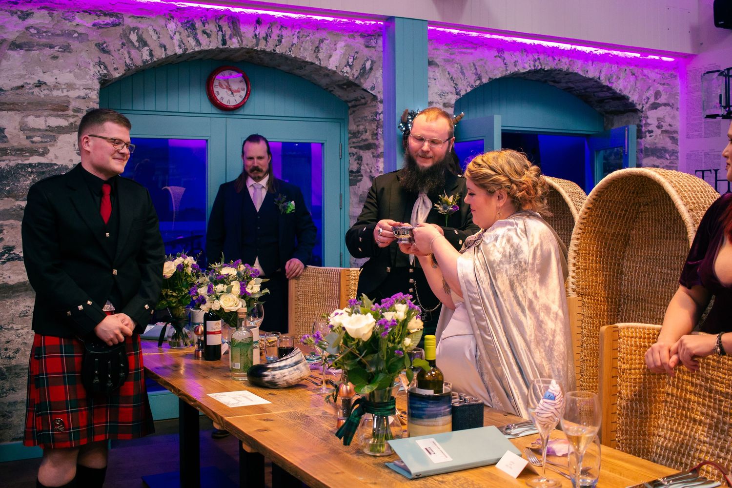 Wedding ceremony in rustic stone venue with guests in Scottish kilts and floral table decorations at the storehouse, kirkwall.