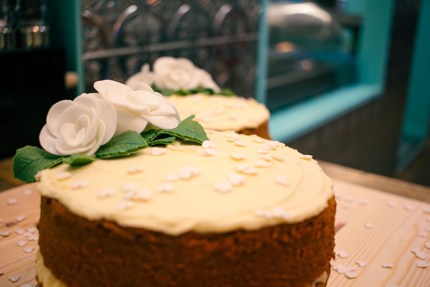 Two elegant white frosted cakes topped with white roses and green leaves on display at a wedding in orkney.