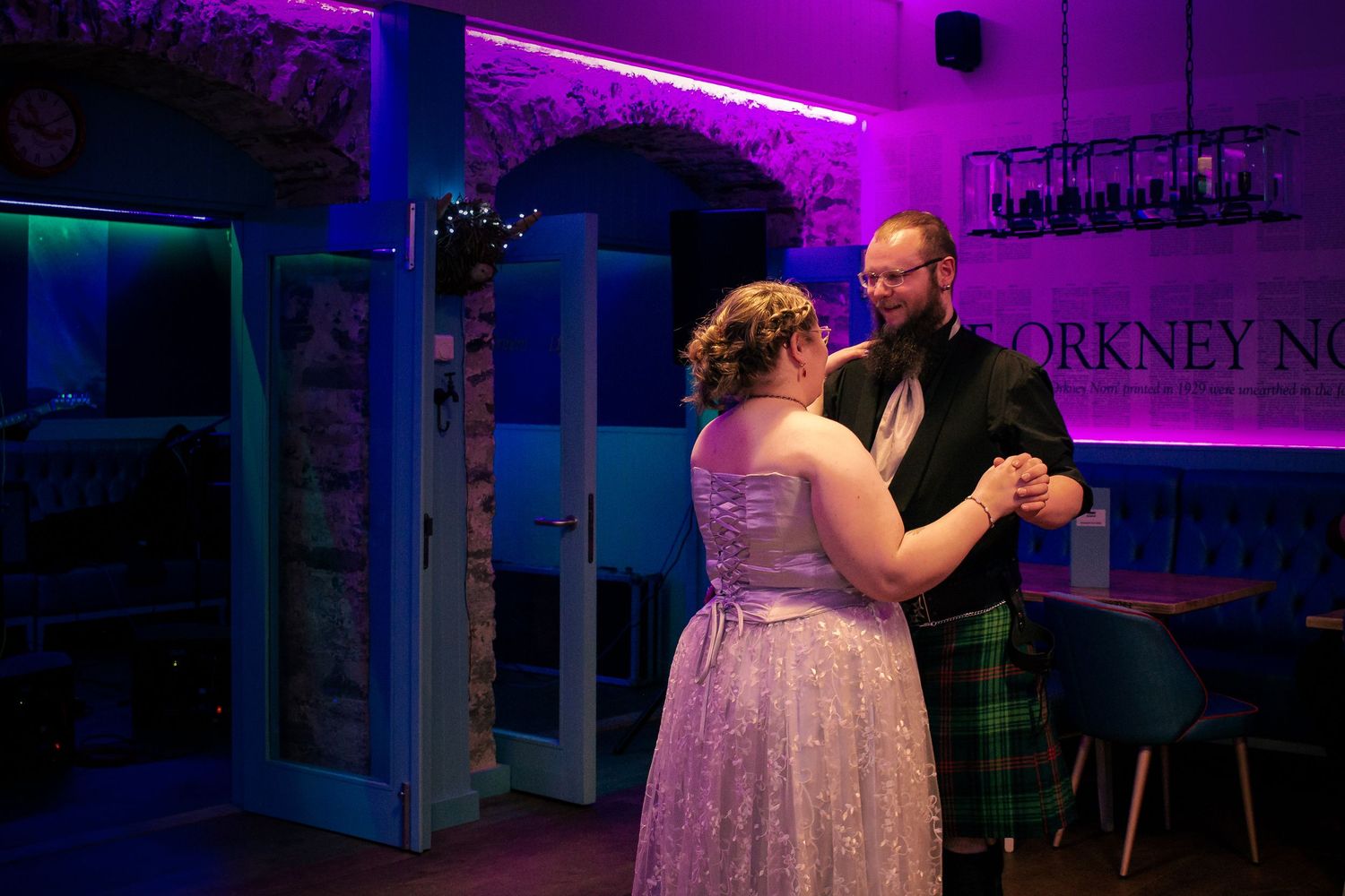 Couple sharing a romantic first dance in a dimly lit venue with purple lighting and Scottish tartan kilt at the storehouse, kirkwall