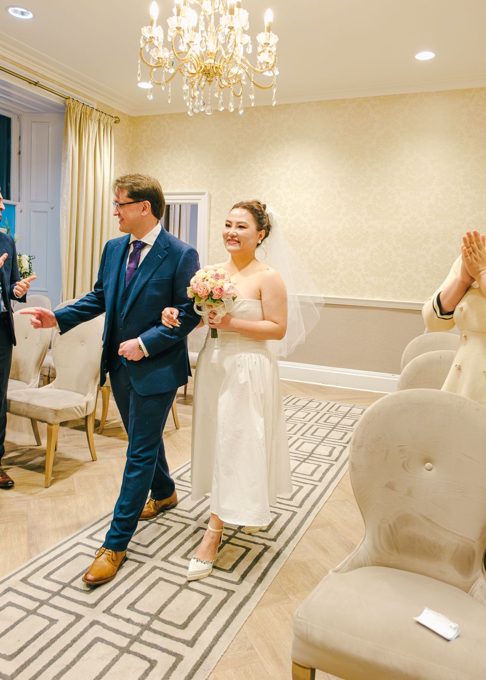 Bride and groom walking down aisle in elegant chandelier-lit wedding ceremony room with guests taken by Orkney Photographer