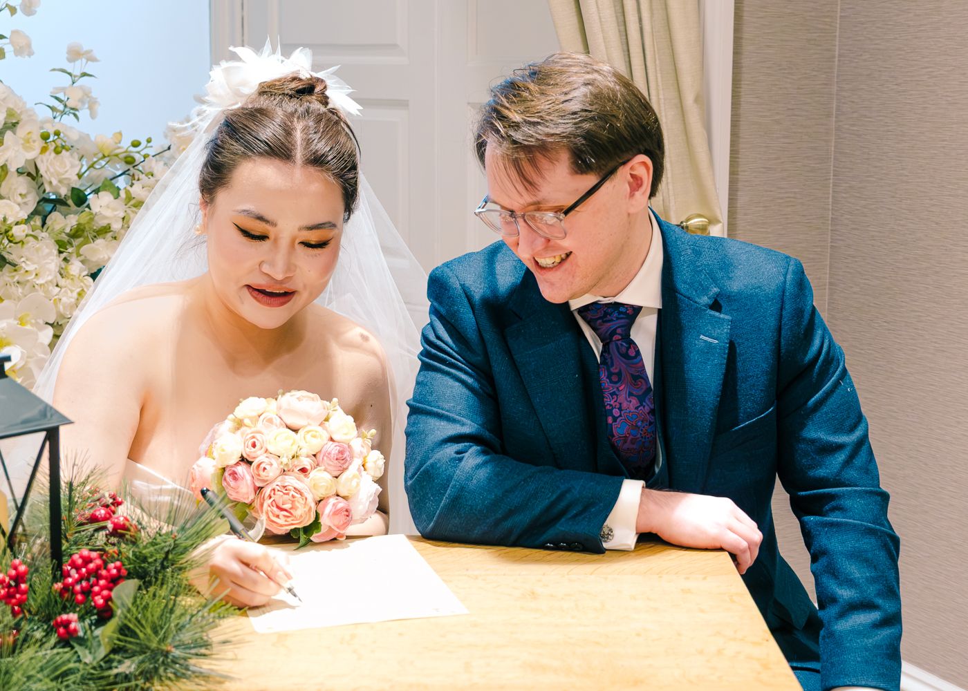 Bride and groom signing wedding register at table, bride holding pink and white floral bouquet taken by Orkney Photographer