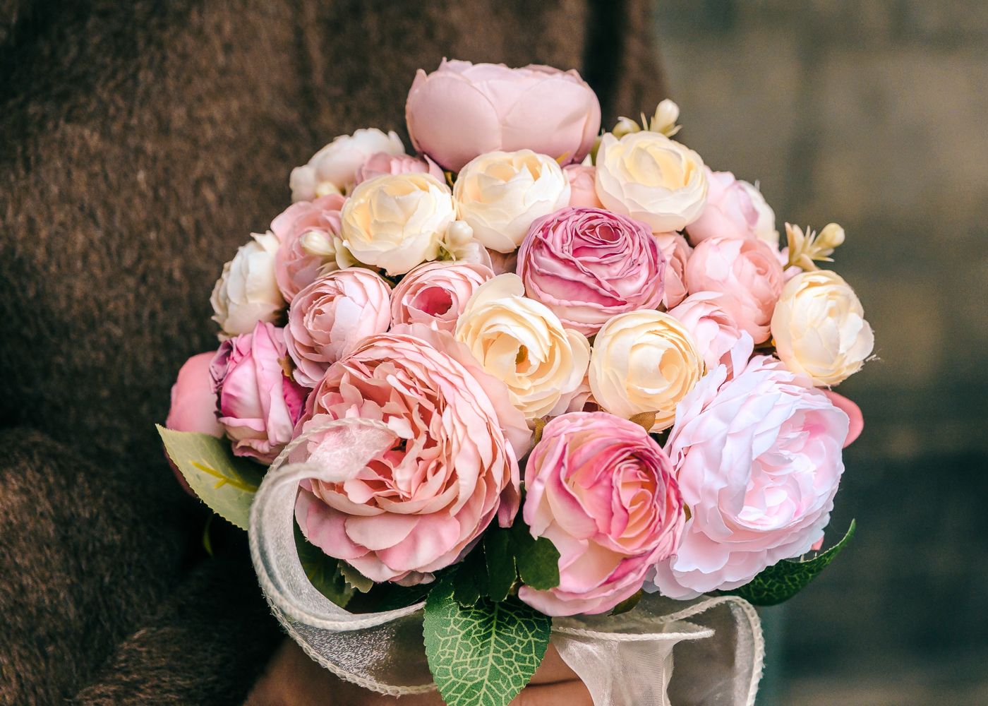 Romantic bridal bouquet of pink and cream roses and peonies held by a person in a brown coat taken by Orkney Photographer