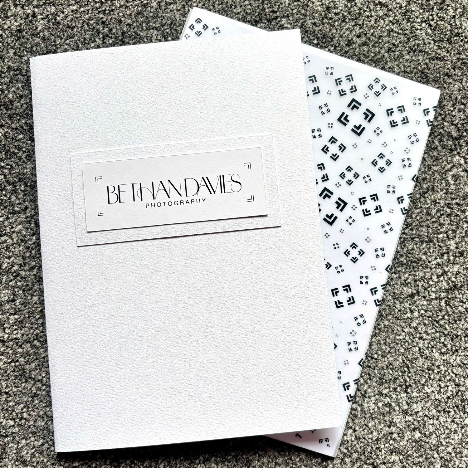 White photography portfolio booklet with Bethan Davies Photography logo and decorative patterned tissue paper on gray background.