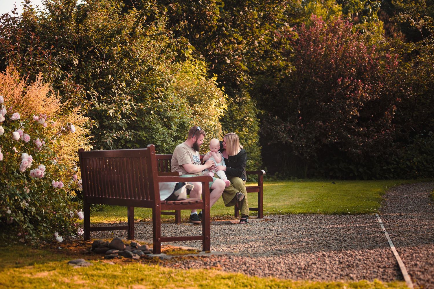 Family sitting together on a wooden garden bench surrounded by colorful autumn trees and lush greenery  by Orkney Family Photographer