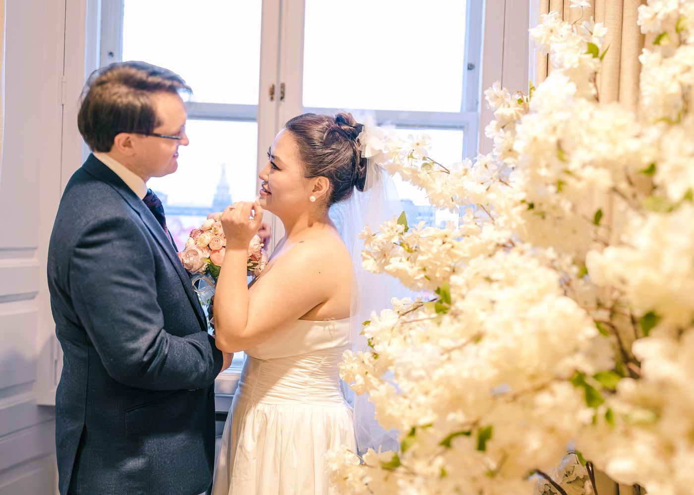 Joyful bride and groom sharing a tender moment surrounded by white cherry blossom branches indoors taken by Orkney Photographer