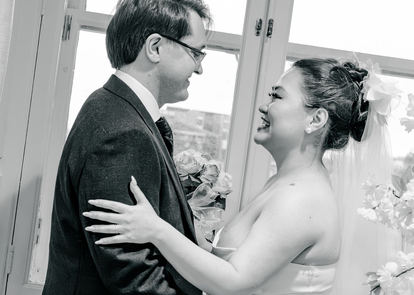 Black and white wedding photo of smiling bride and groom embracing near a bright window taken by Orkney Photographer