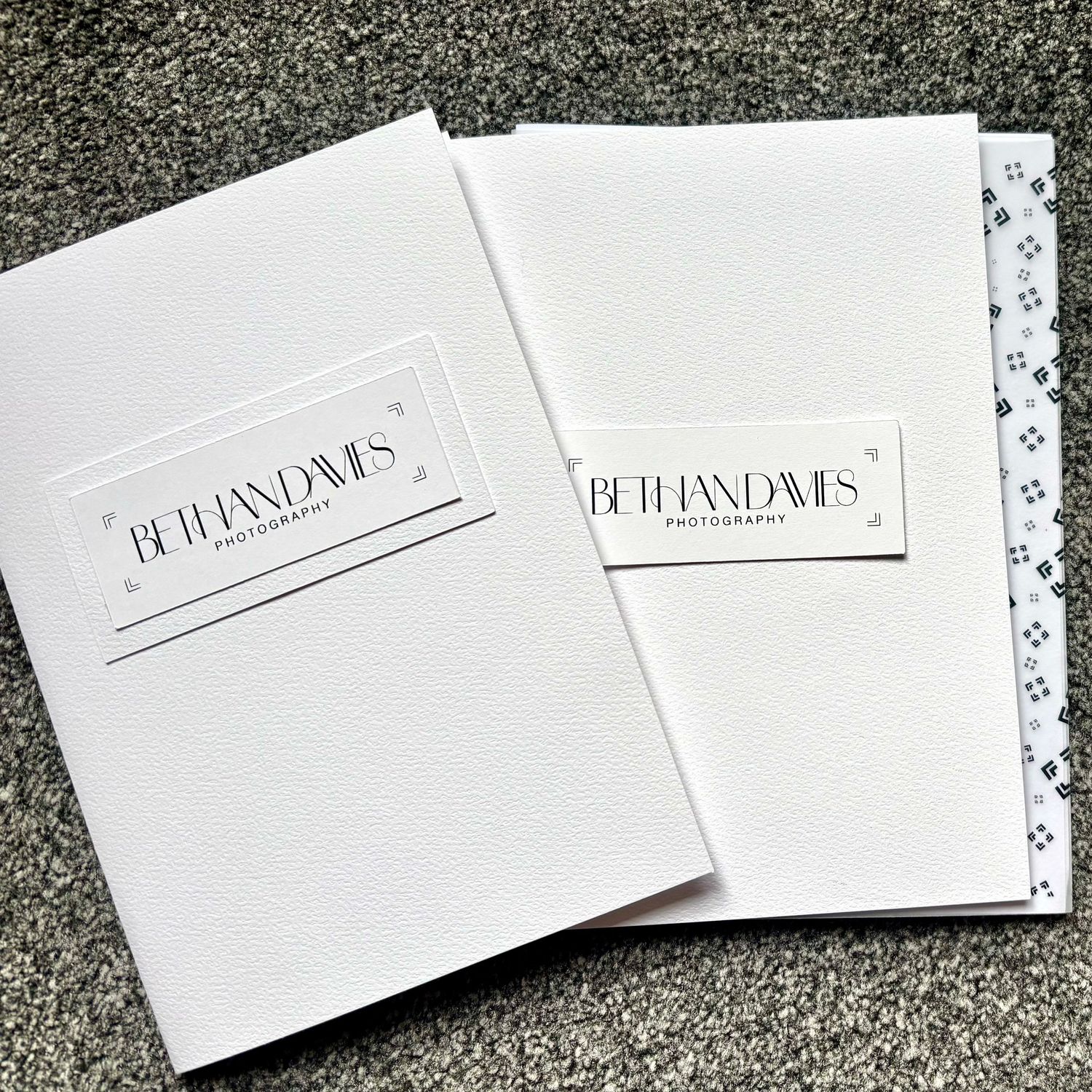 Two white Beth Davis Photography branded folders with elegant embossed logo design displayed on gray background.