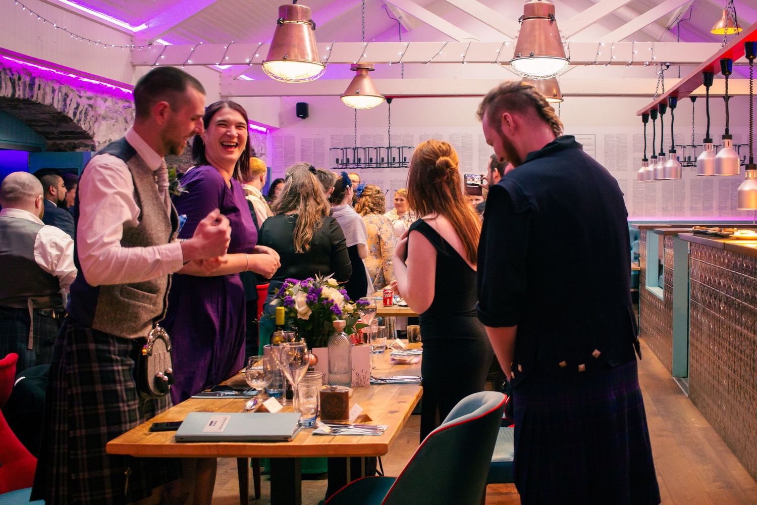 Guests in Scottish kilts socializing at an elegant indoor wedding reception with floral centerpieces at the storehouse, kirkwall.
