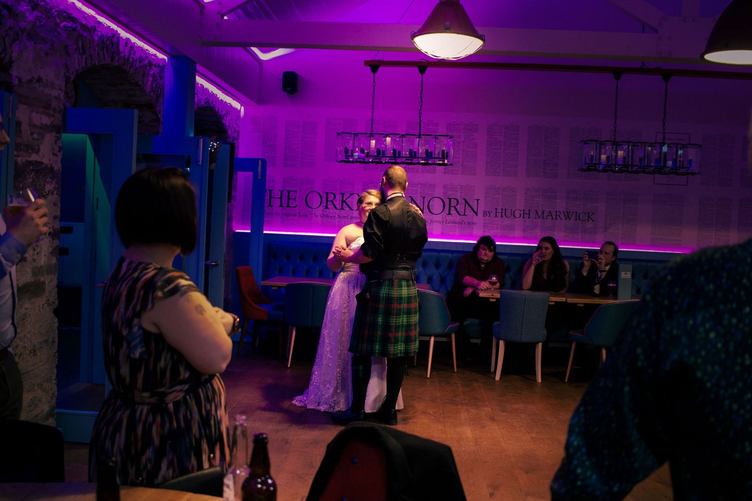Couple dancing in Scottish attire at Tat the storehouse, kirkwall with purple neon lighting.
