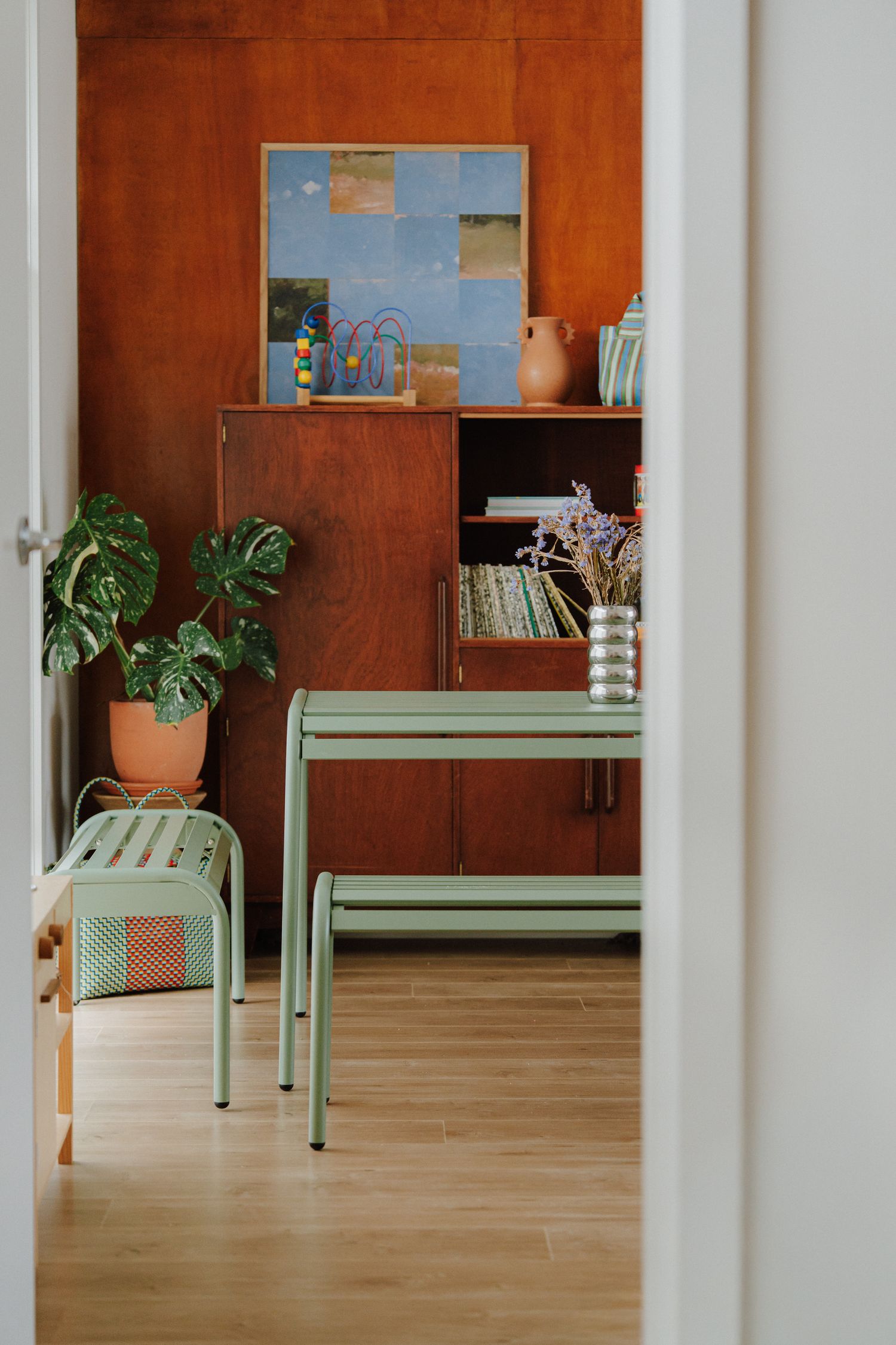 Mint green dining table and bench set in a room with vintage wooden cabinet and houseplants.