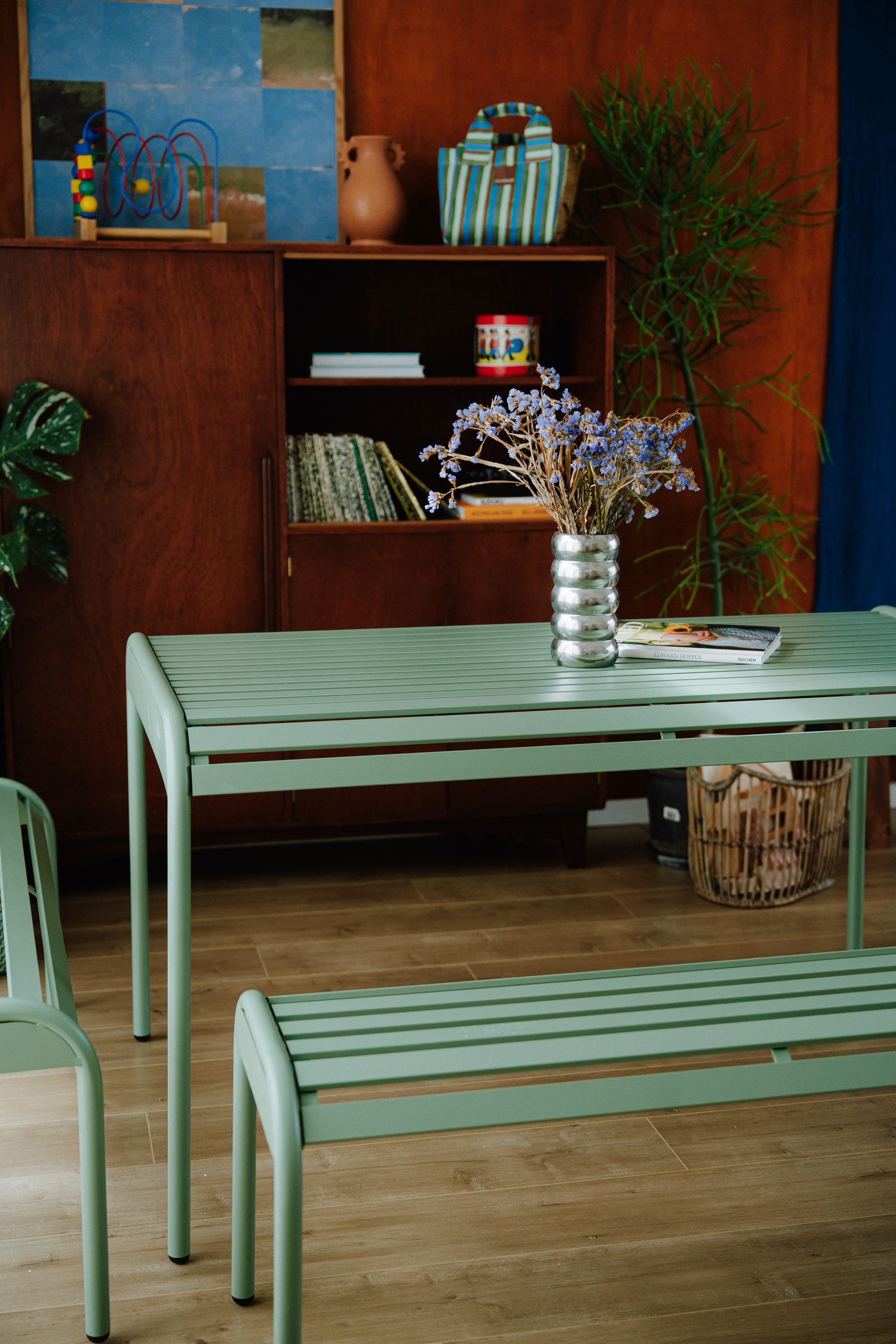 Mint green outdoor-style dining table and bench with dried flower vase in a retro-inspired interior.