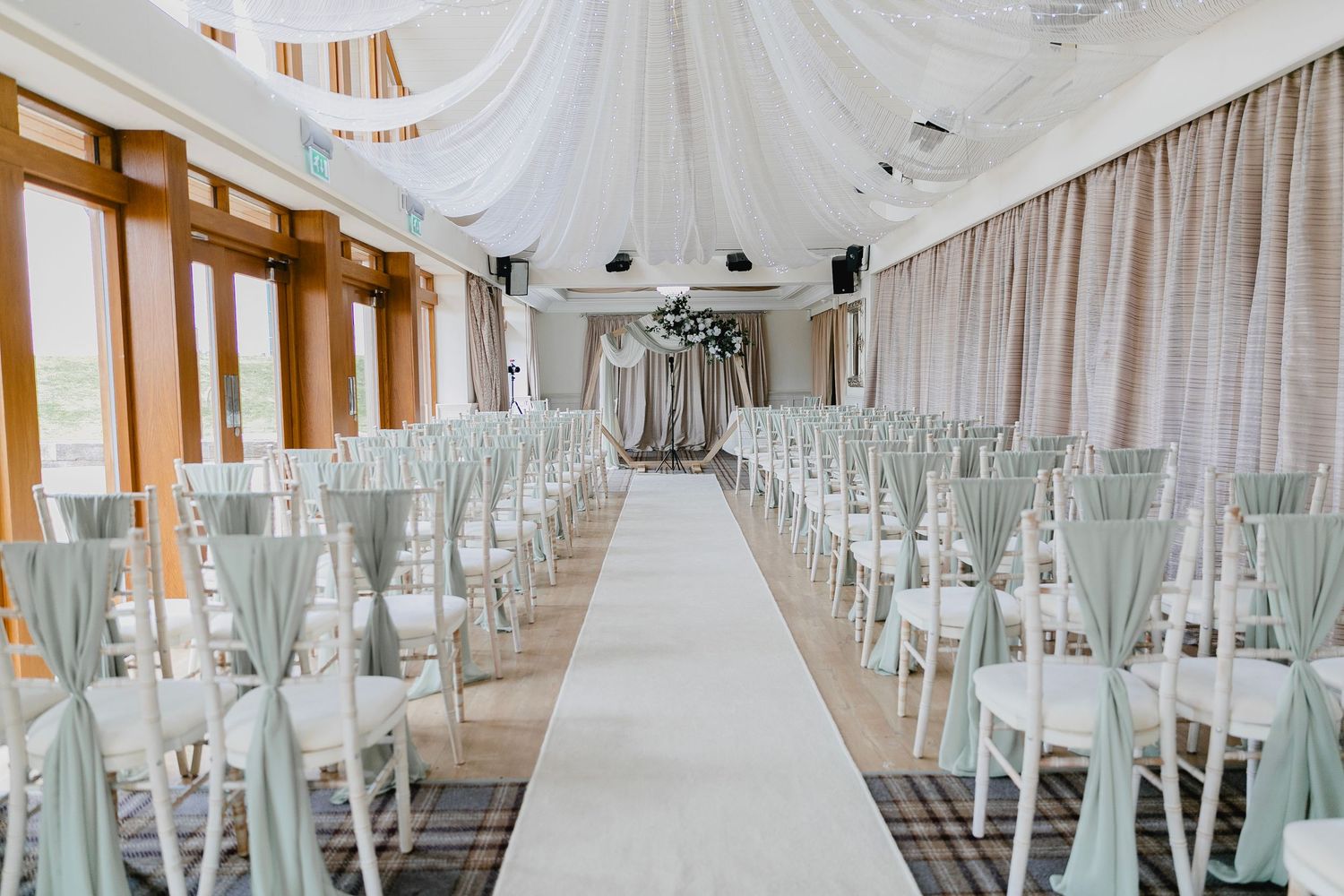 Elegant wedding ceremony venue with sage green chair sashes and white draped ceiling decor.