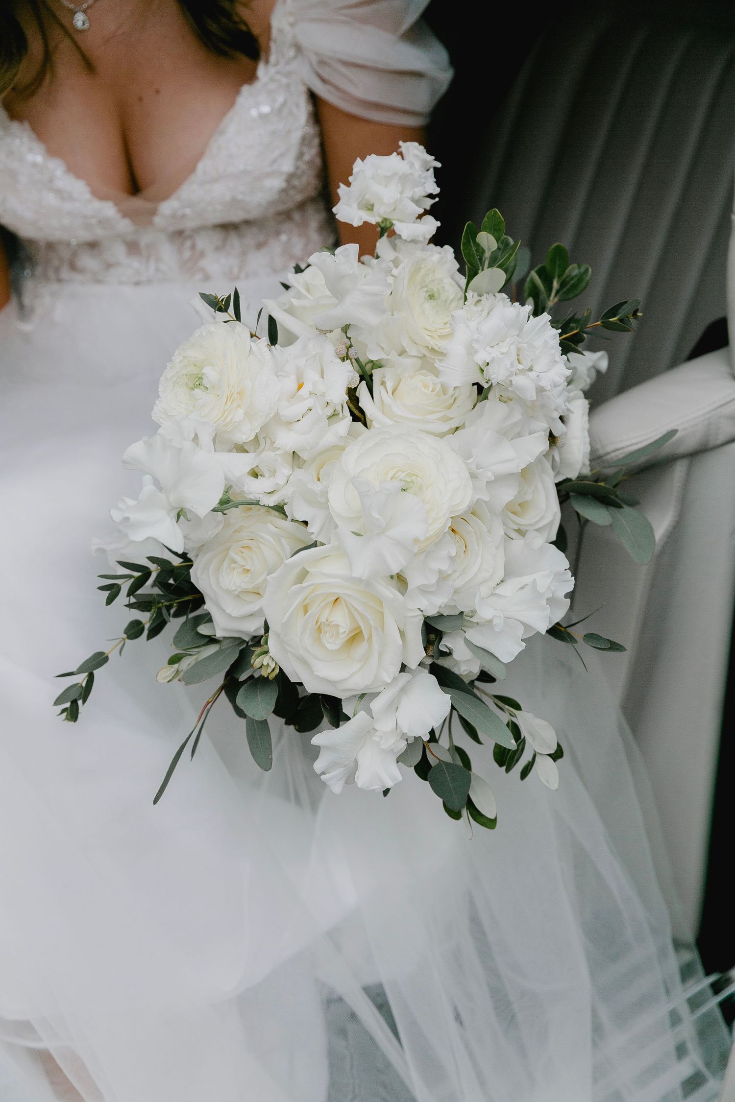 Bride holding elegant white rose and greenery wedding bouquet in lace gown.