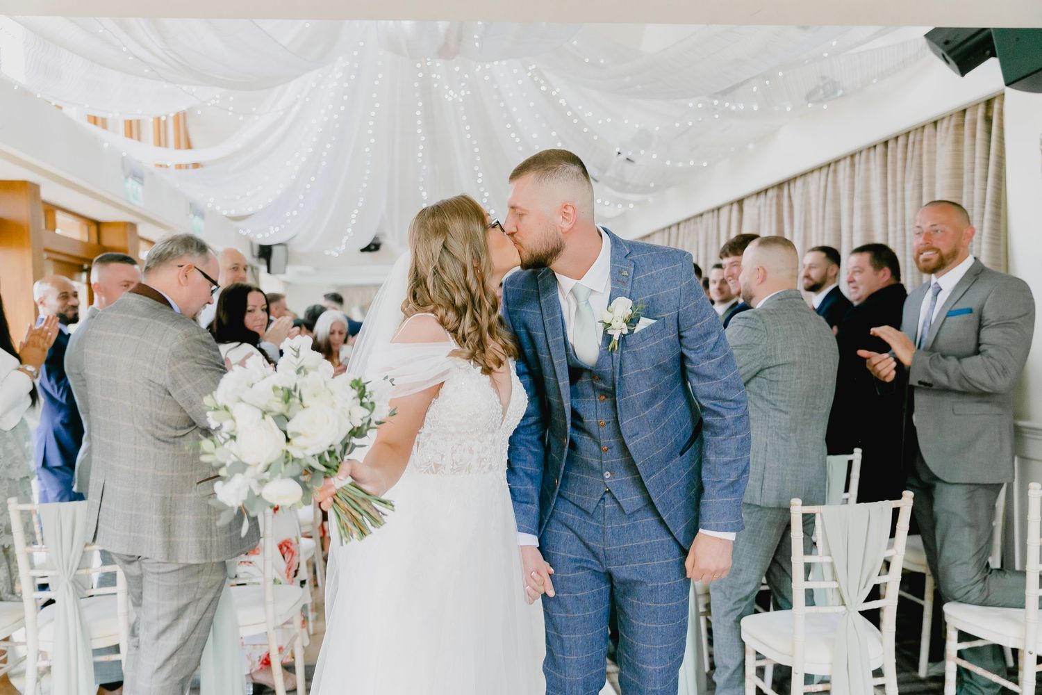 Bride and groom sharing first kiss at wedding ceremony under draped white canopy.