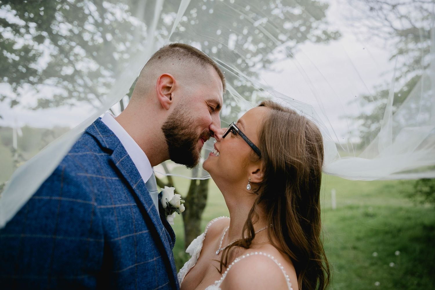Bride and groom sharing intimate moment under wedding veil in outdoor garden setting.