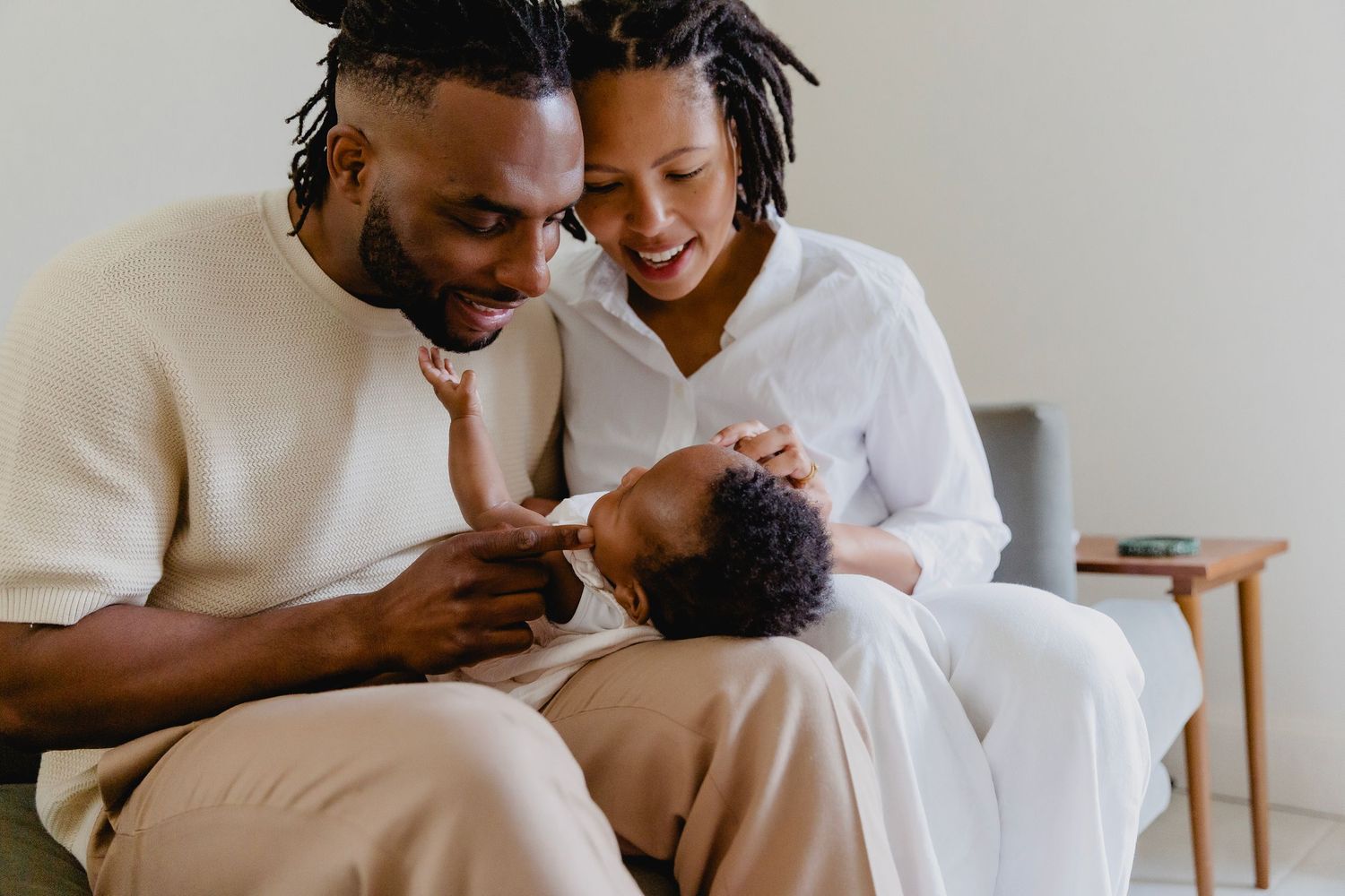 Happy Black couple sitting on sofa smiling and bonding with their newborn baby.