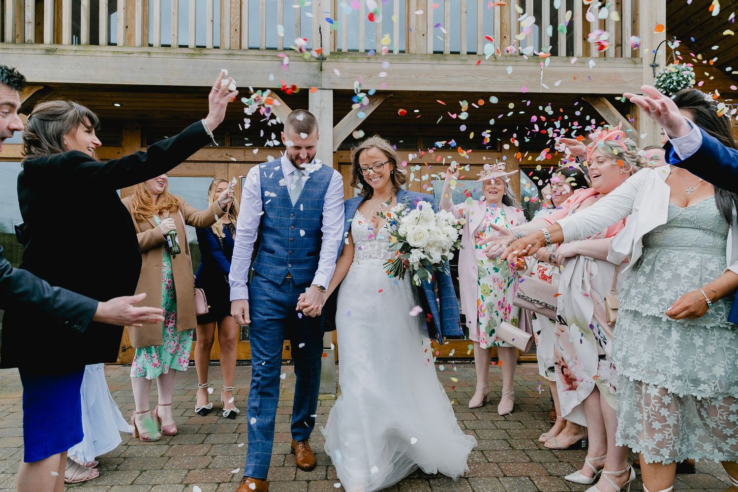 Bride and groom walking through colorful confetti shower with cheering wedding guests.