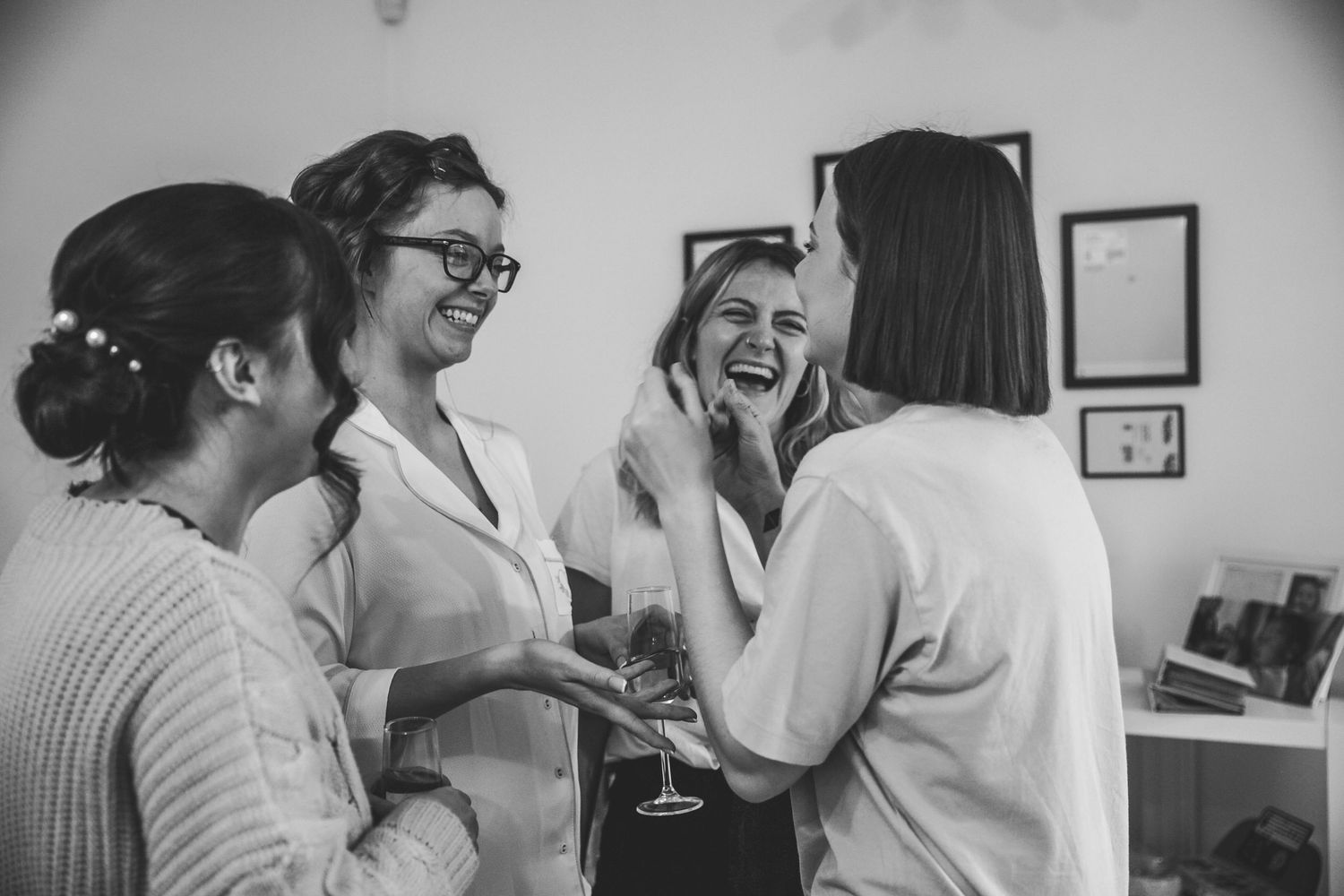 Bridesmaids laughing and celebrating together during bridal preparations in black and white photo.