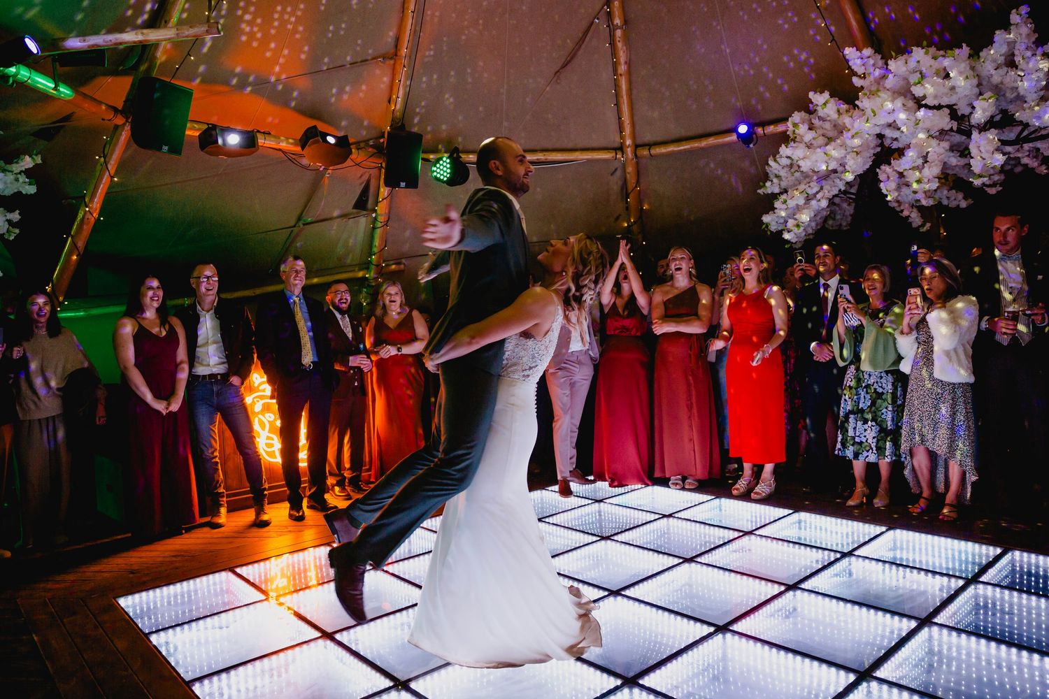 Bride and groom share first dance on illuminated LED floor inside decorated tipi reception.