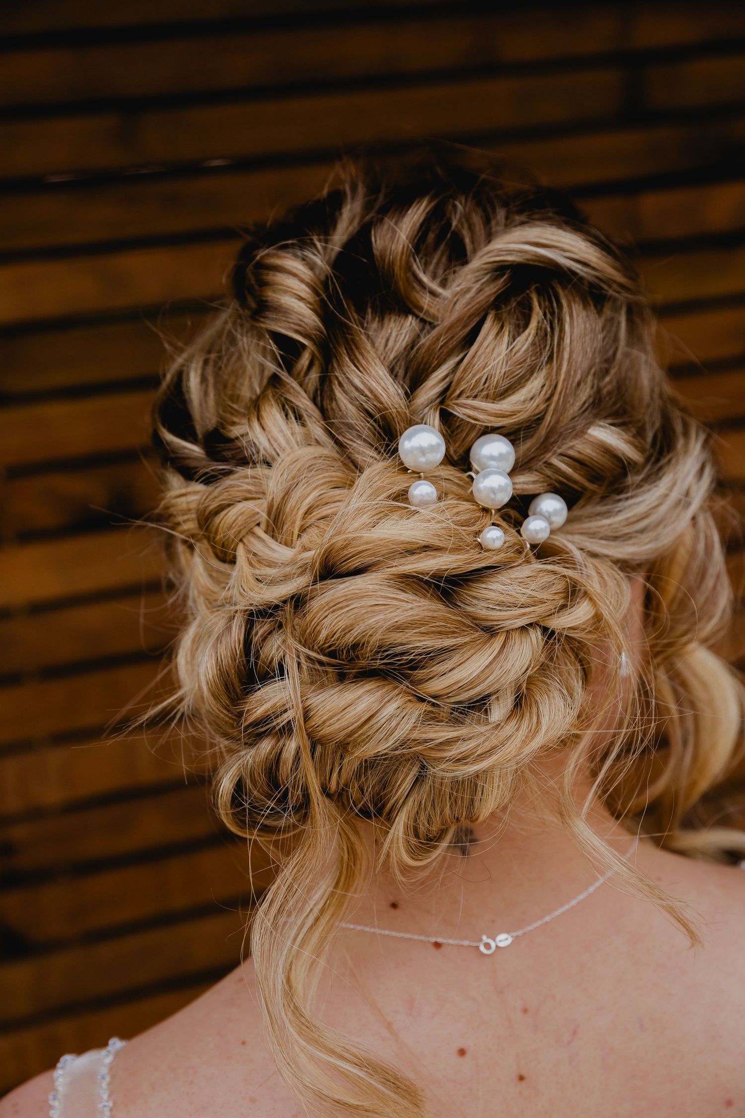 Elegant bridal updo with braided bun and pearl hair pins against a wooden background.