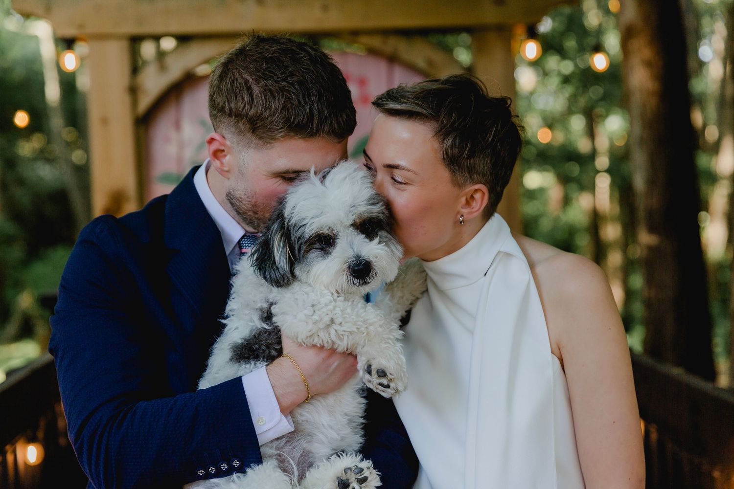 Newlywed couple kissing fluffy black and white dog