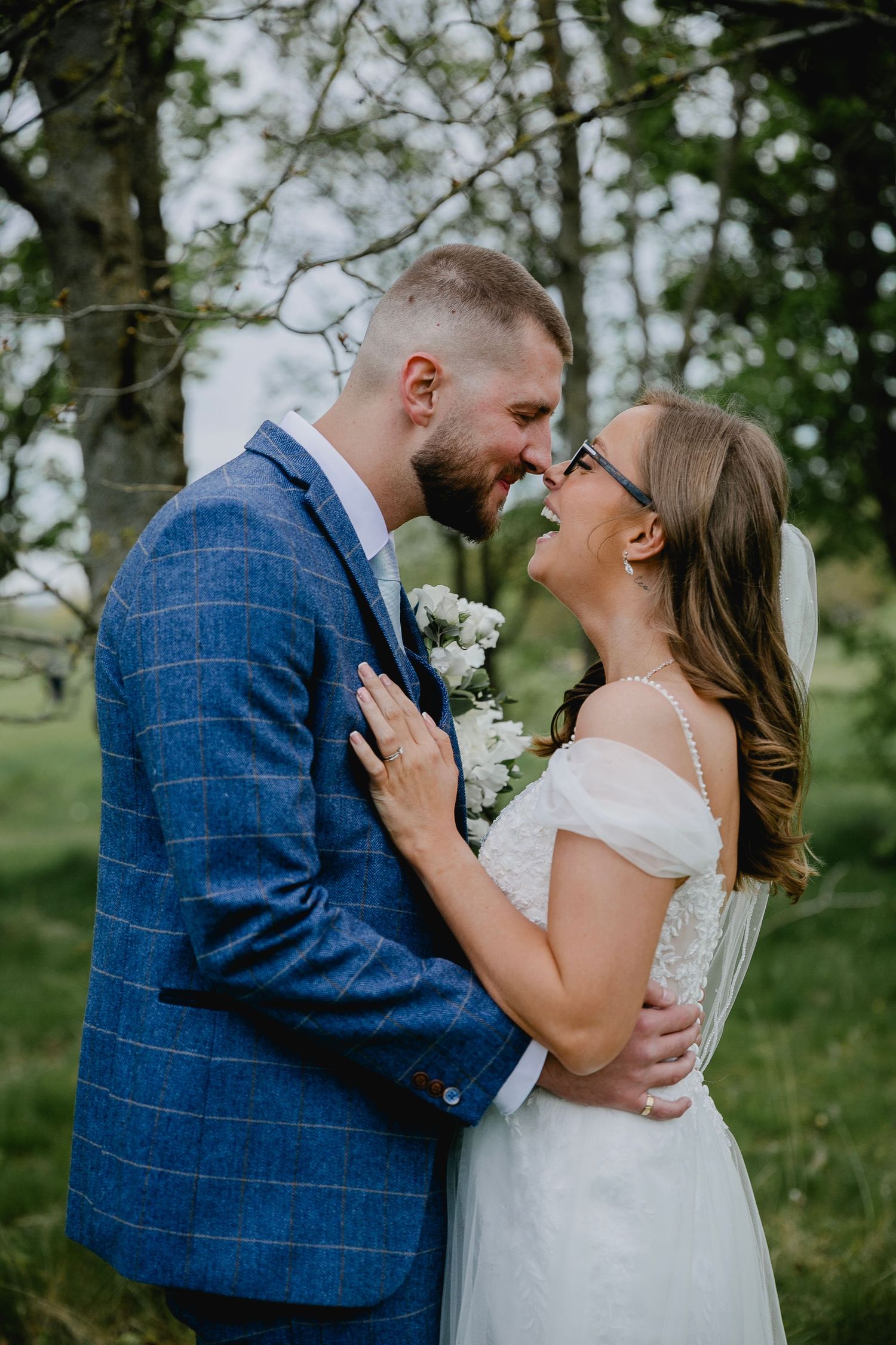 Bride and groom sharing a romantic moment outdoors, nearly kissing in a lush green setting.