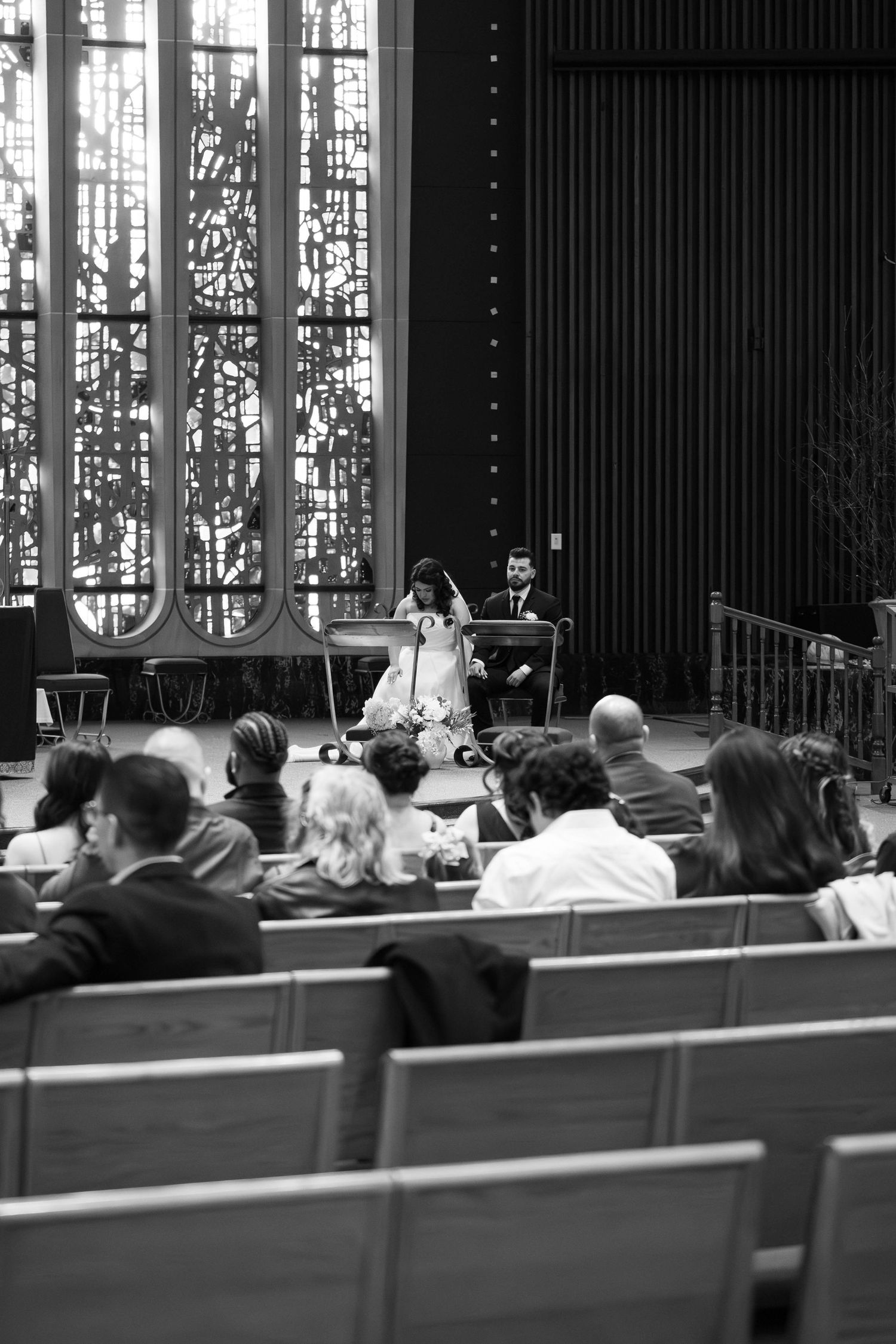 Black and white church wedding ceremony with guests seated in pews facing altar.