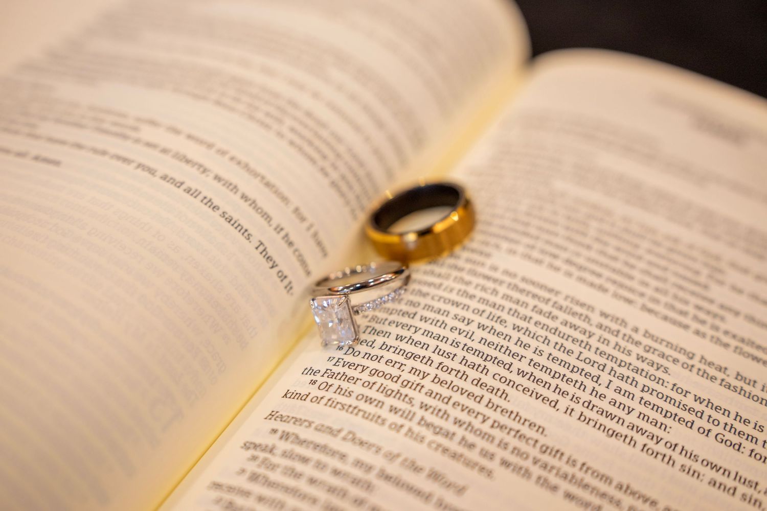 Gold wedding band and diamond engagement ring resting on open Bible pages, symbolizing faith and marriage.