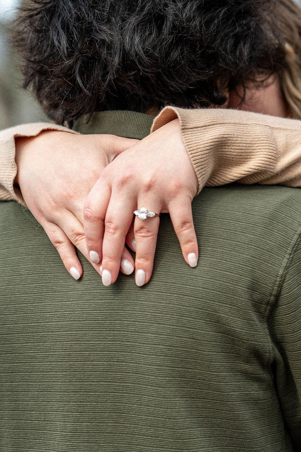 Close-up of a woman's hand with an engagement ring resting on a man's shoulder during a romantic embrace.