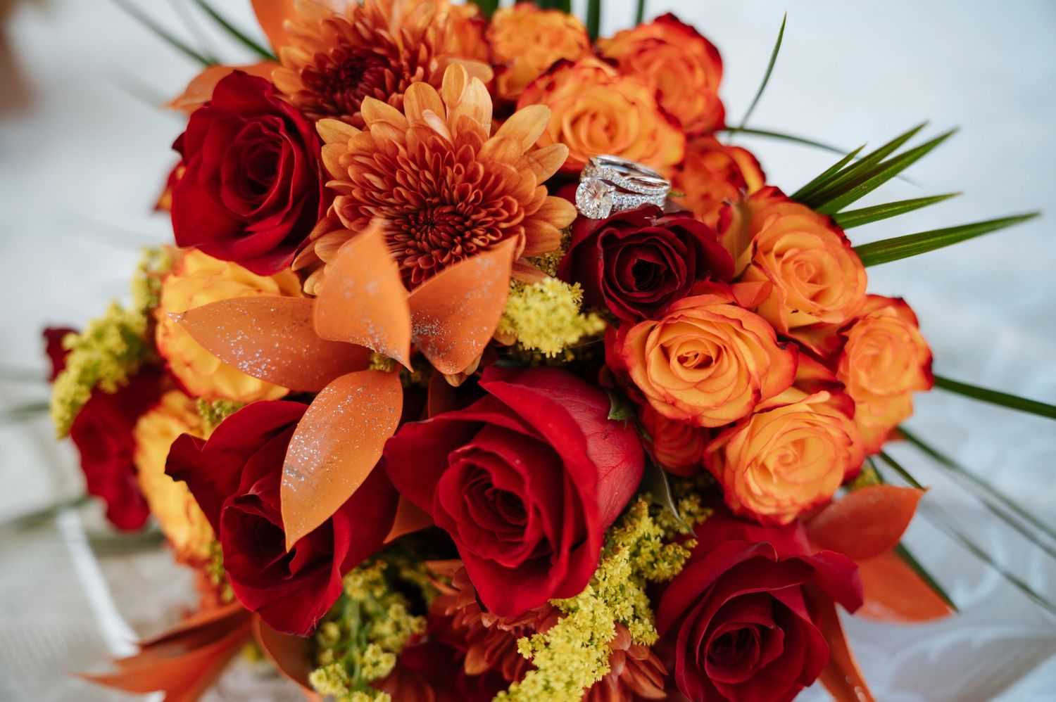 Vibrant bridal bouquet of red and orange roses with a diamond engagement ring resting on top.