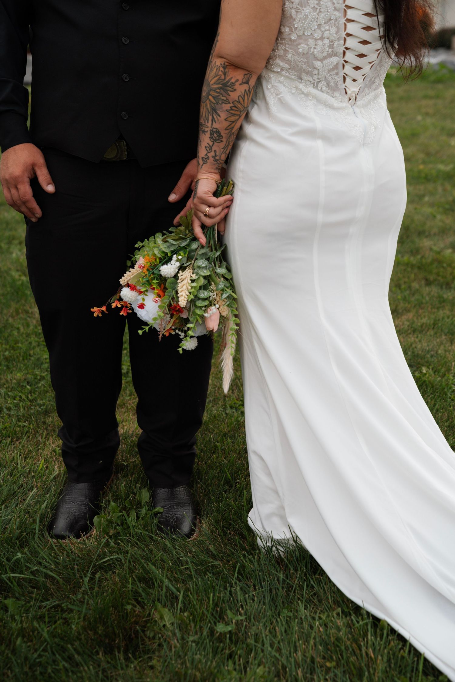Bride and groom holding wildflower bouquet standing together on grass at outdoor wedding.