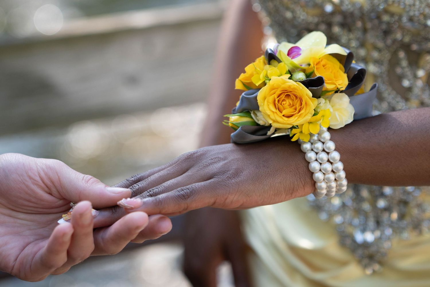 Close-up of yellow rose wrist corsage with pearl bracelet on prom date's wrist during corsage pinning.