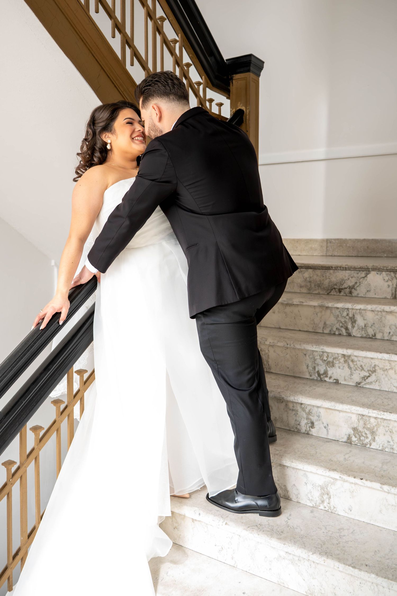 Bride and groom sharing a romantic moment on marble staircase with ornate railing on wedding day.