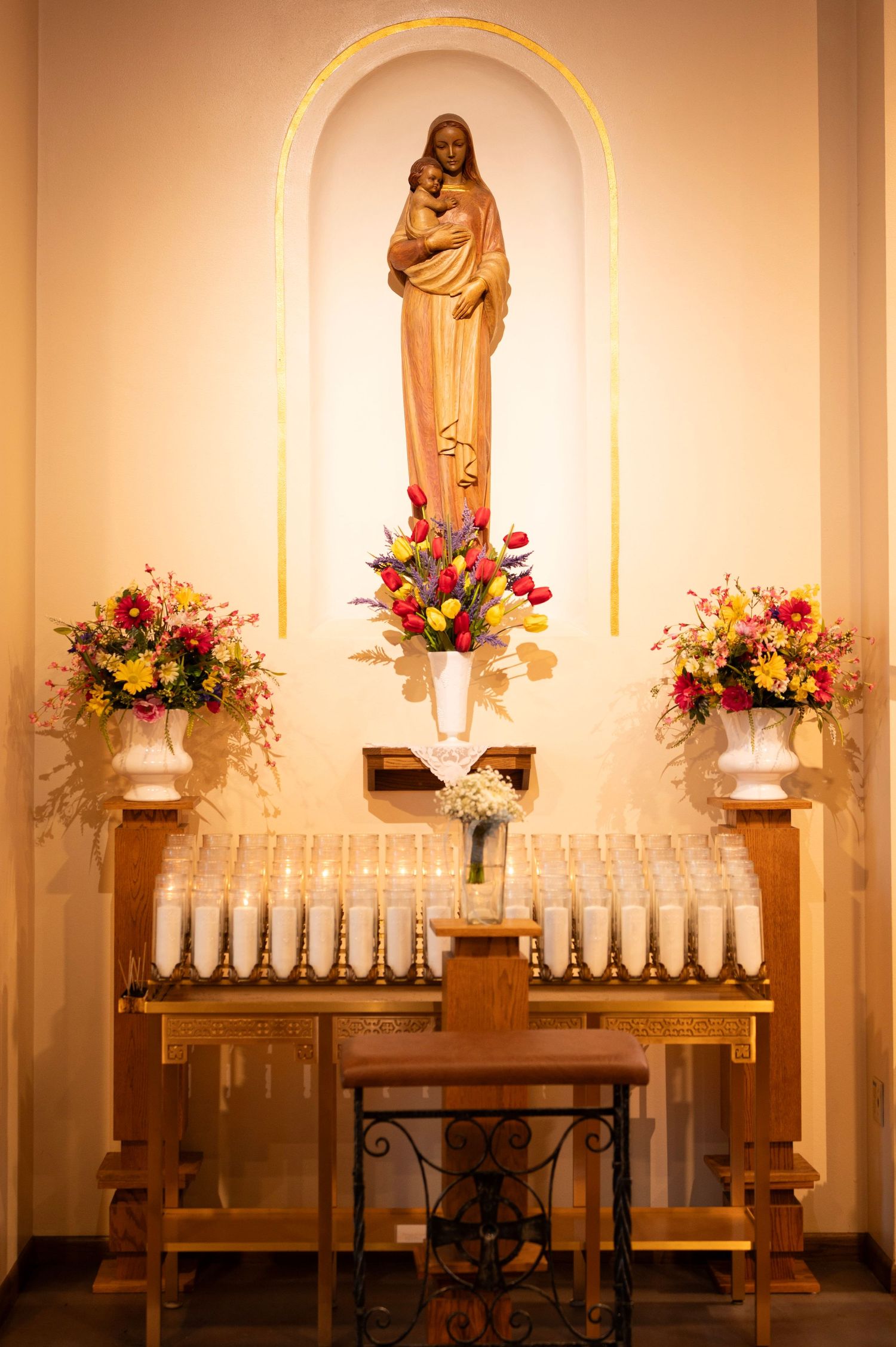 Catholic church altar with Virgin Mary statue, candles, and colorful floral arrangements.