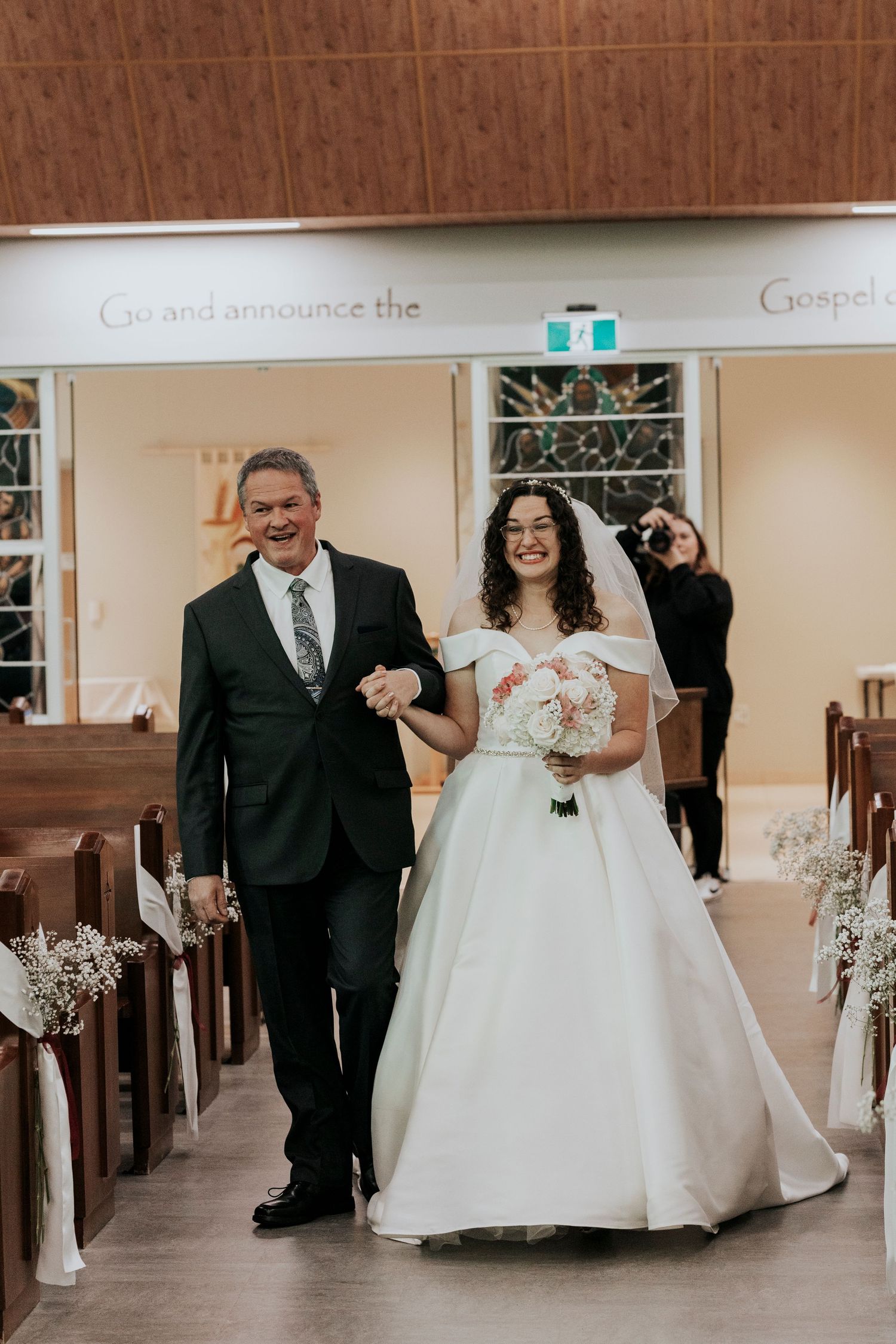 A wedding processional in a chapel with white flowers lining the aisle.