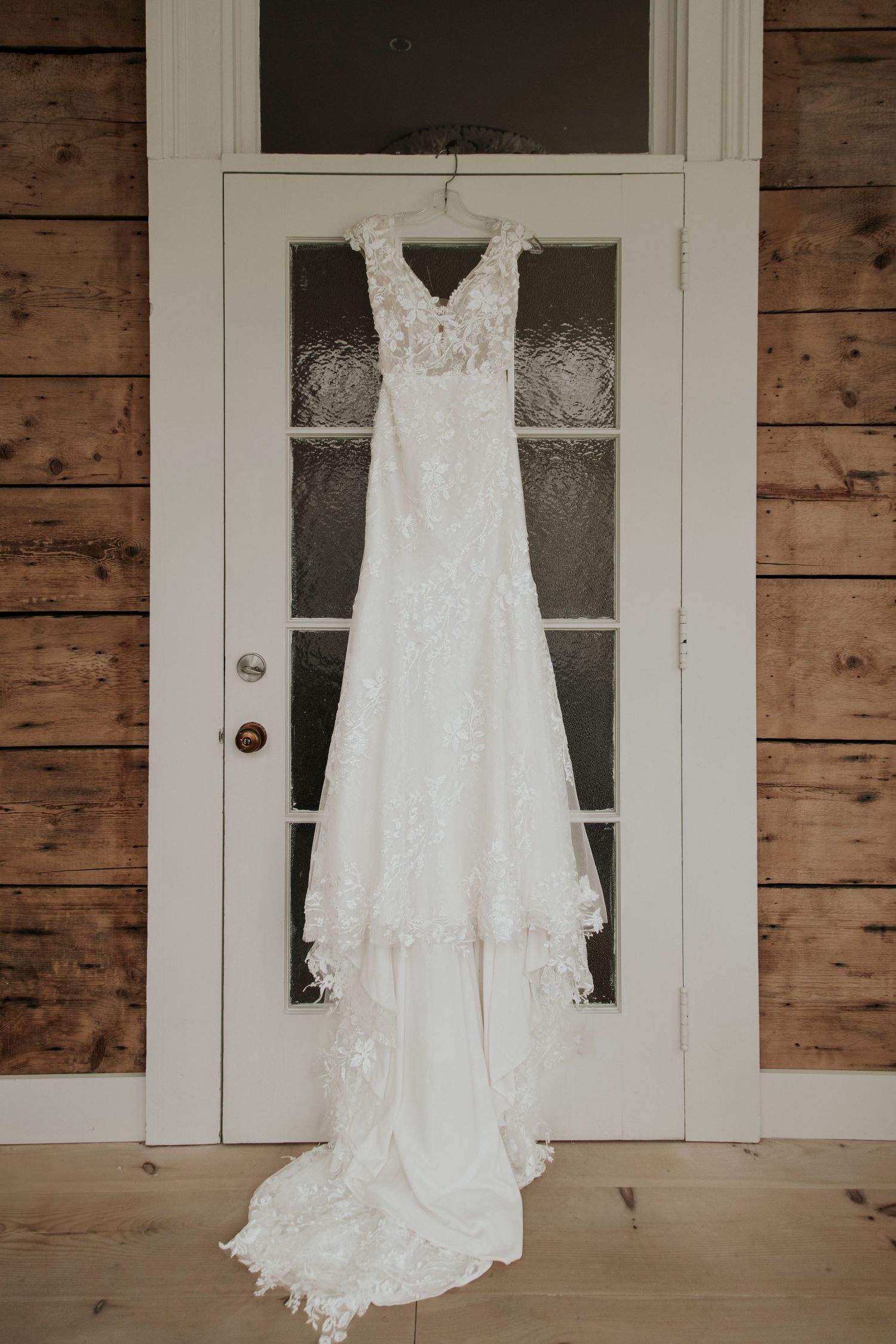Vintage lace wedding dress hanging on white door with glass panels.