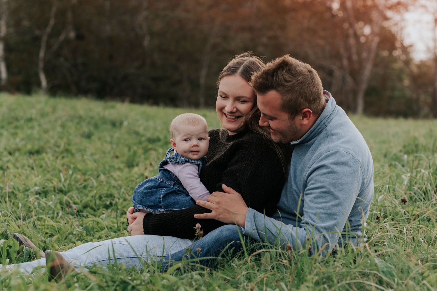 Happy family with baby sitting together in green grassy field.