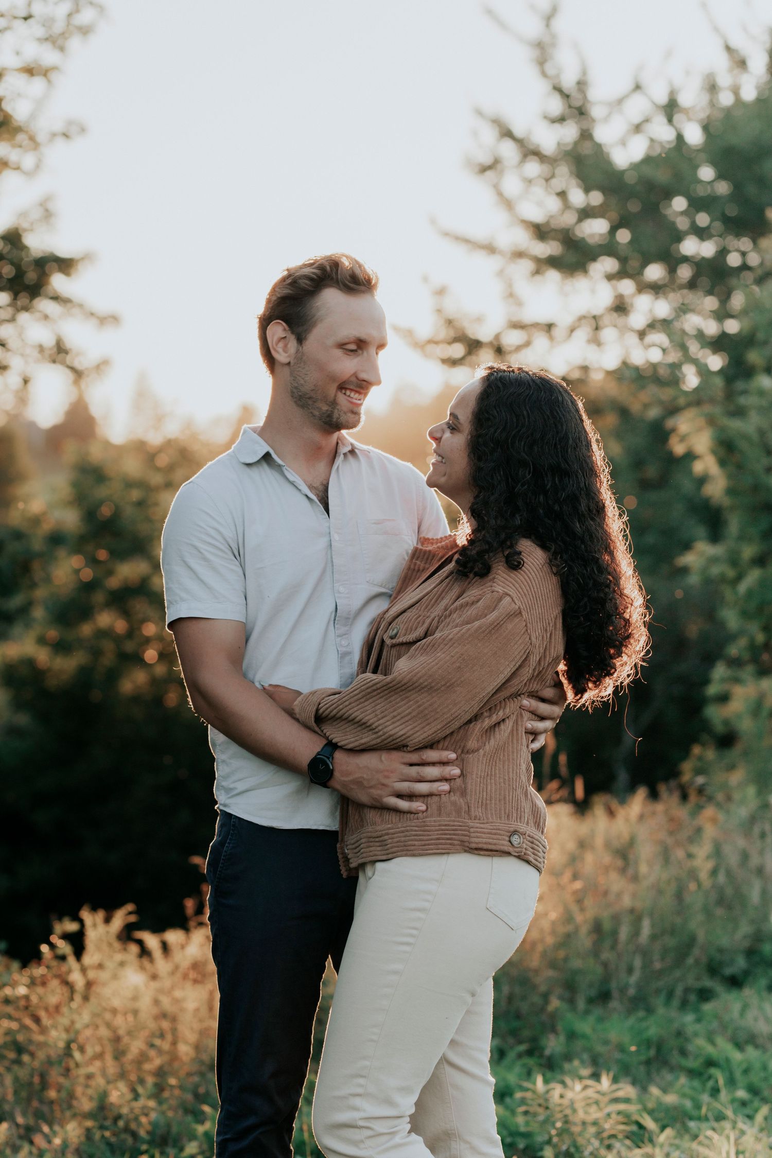 Couple embracing and gazing at each other in a golden sunlit field during an engagement shoot.