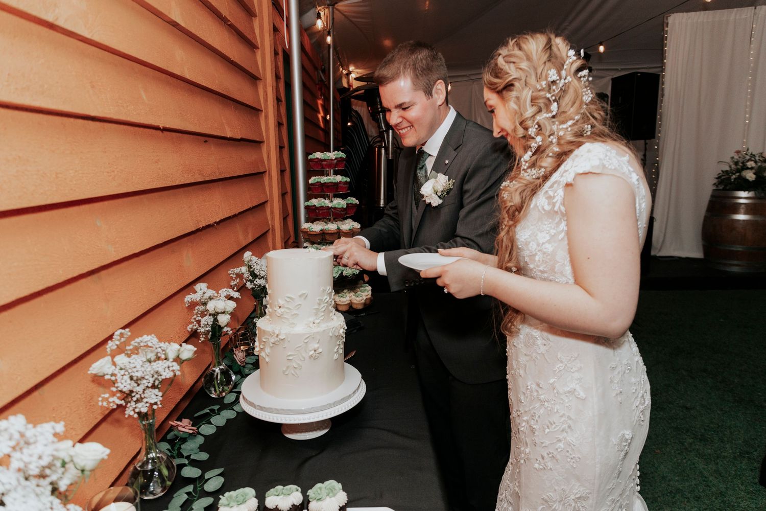 Couple cuts their elegant white wedding cake together at outdoor reception.