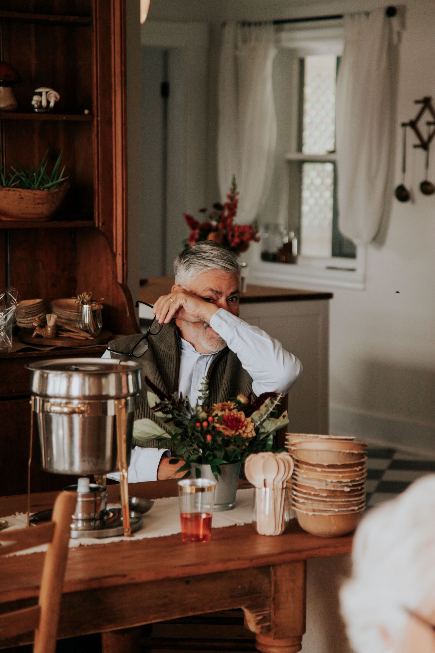 Person sitting at rustic wooden table overcome with emotion watching a rustic at home wedding.