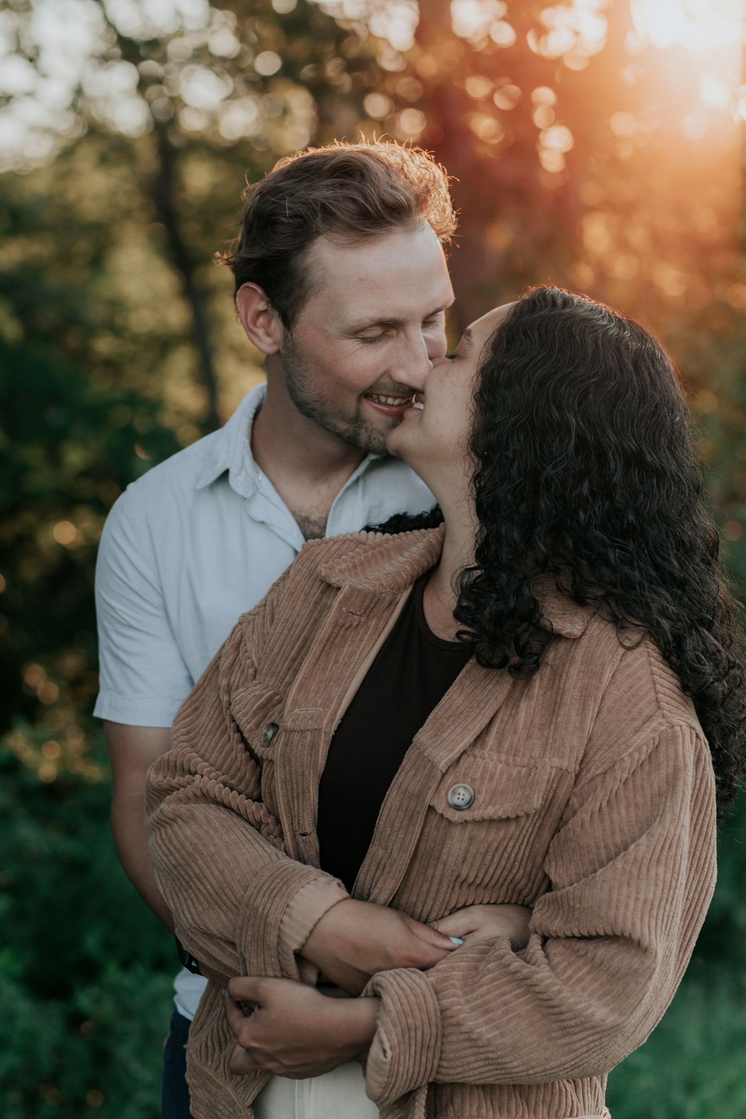 Couple sharing a tender nose kiss while embracing in a sun-drenched outdoor setting at dusk.