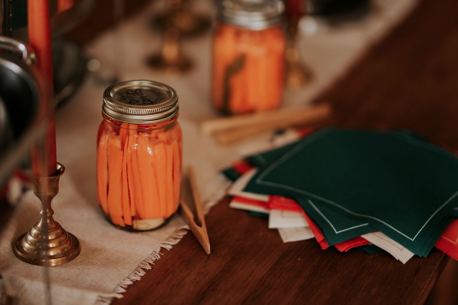 Mason jar with carrot slices sits on a wooden table beside stacked notebooks and a vintage candlestick holder.