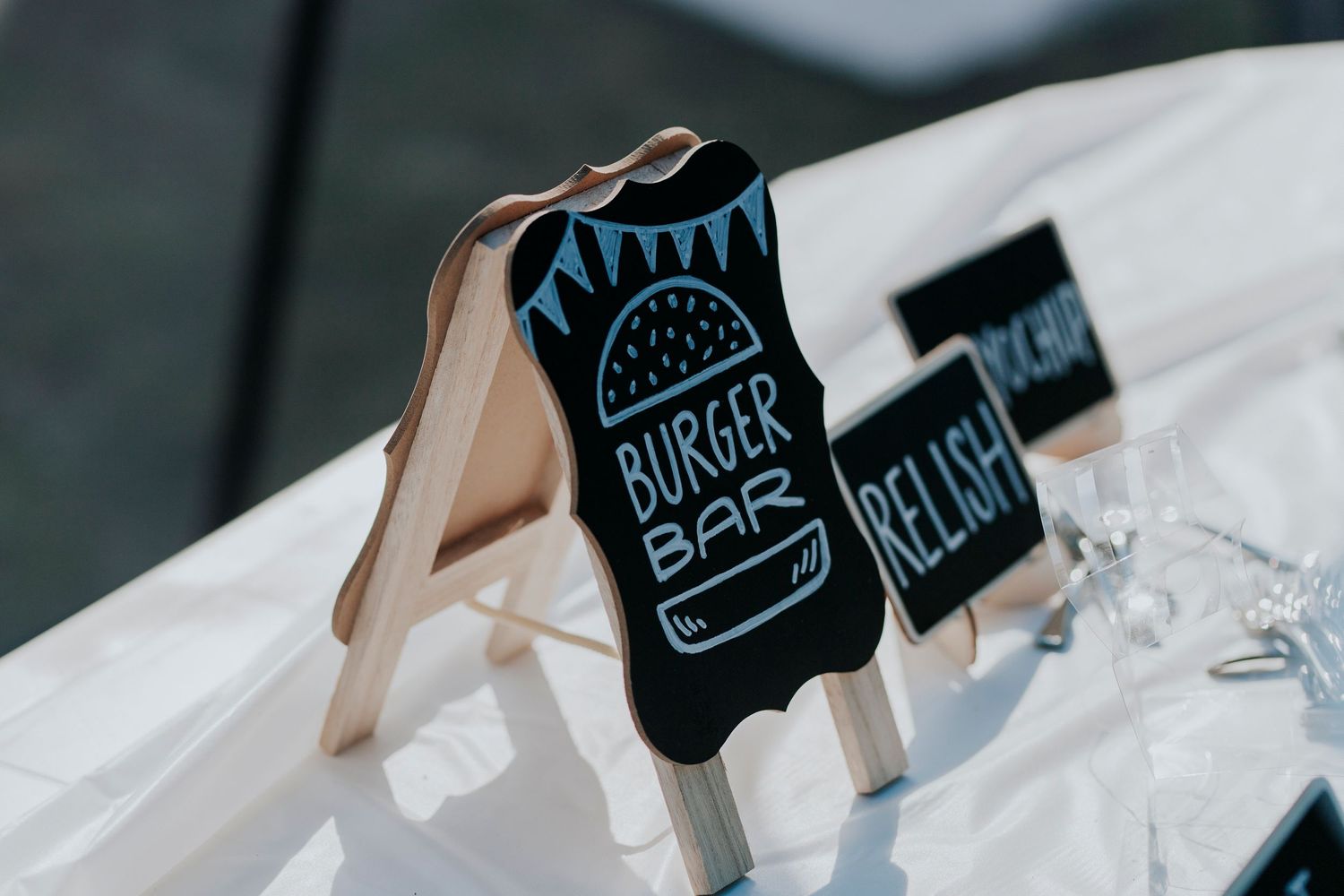 A chalkboard-style sign clip with a burger bar logo drawn on it sits among white linens.