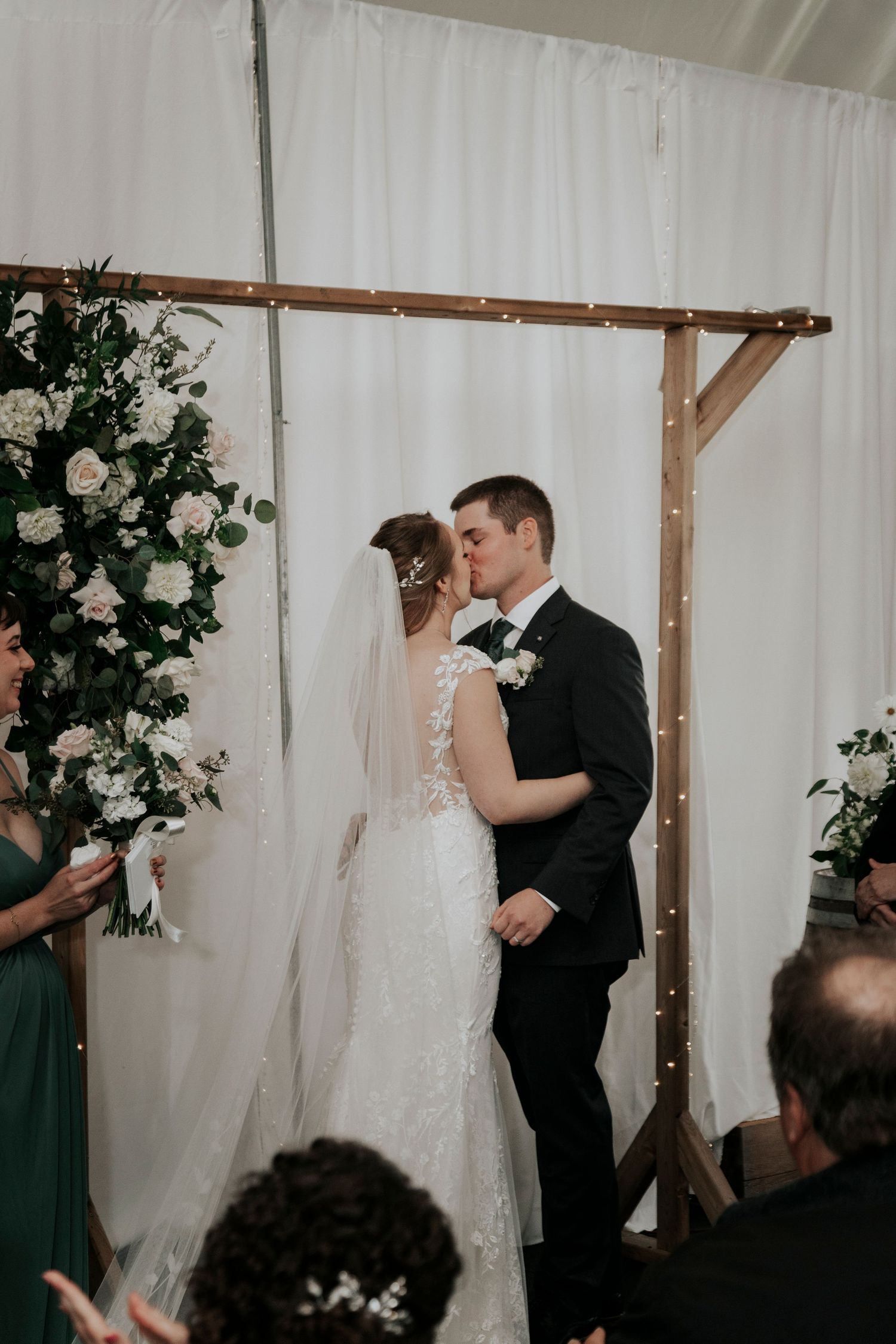Wedding ceremony under a wooden arch decorated with white roses and greenery.