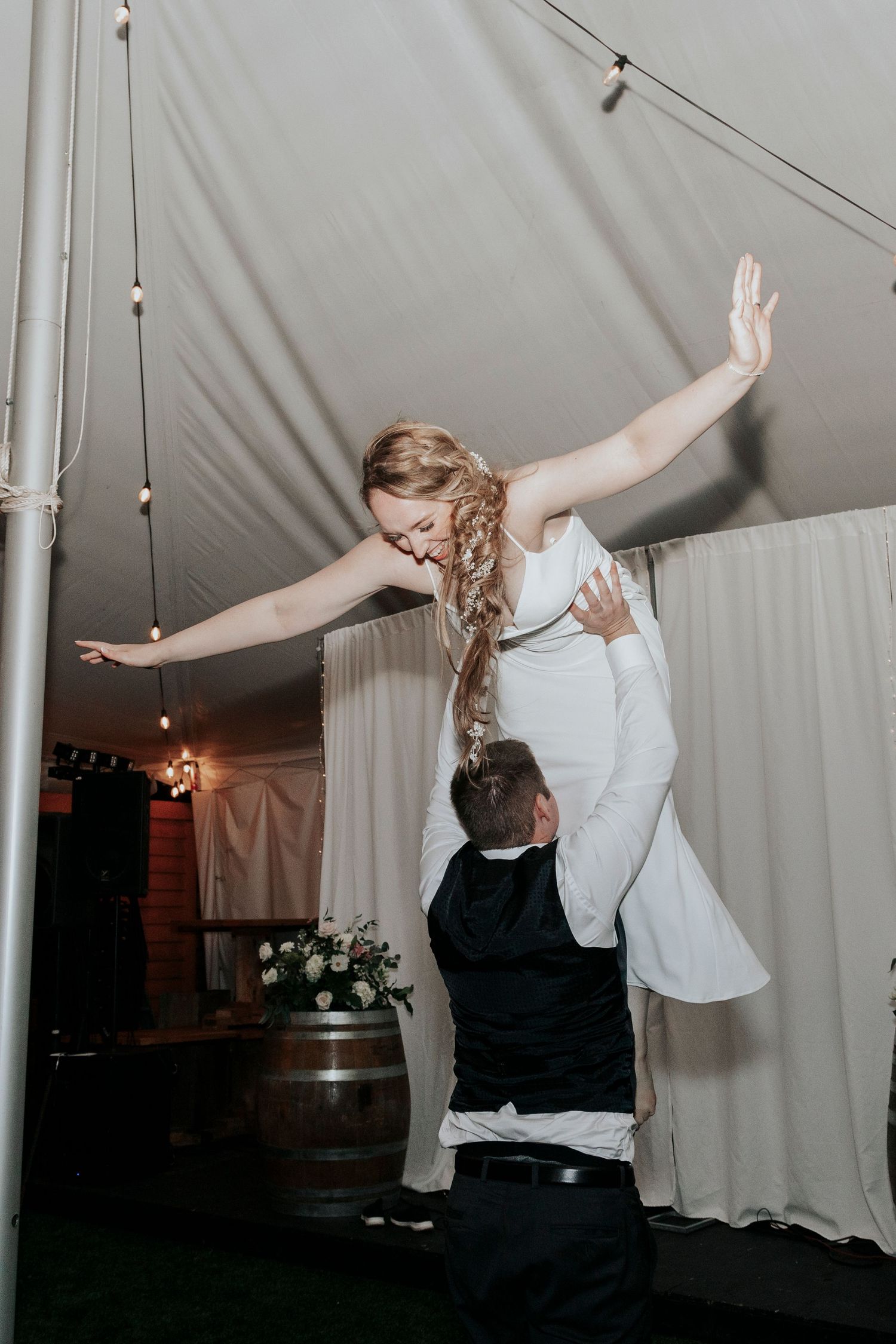 A groom lifting his bride with outstretched arms on a decorated dance floor at a tented reception.