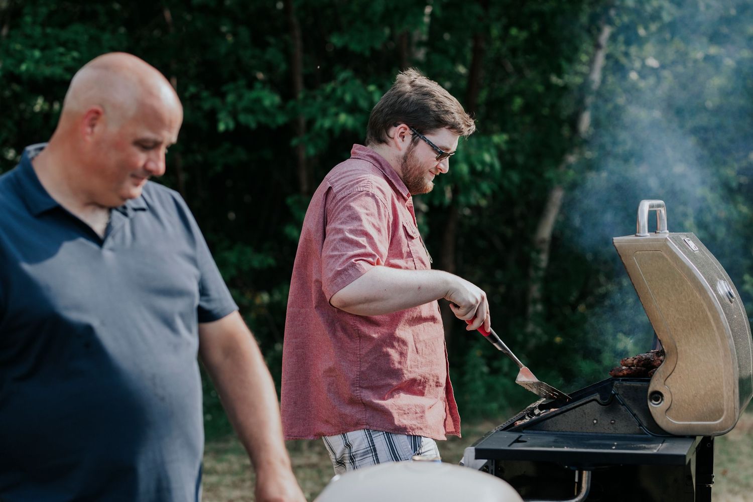 Two people standing at a grill cooking outdoors during a summer barbecue gathering.
