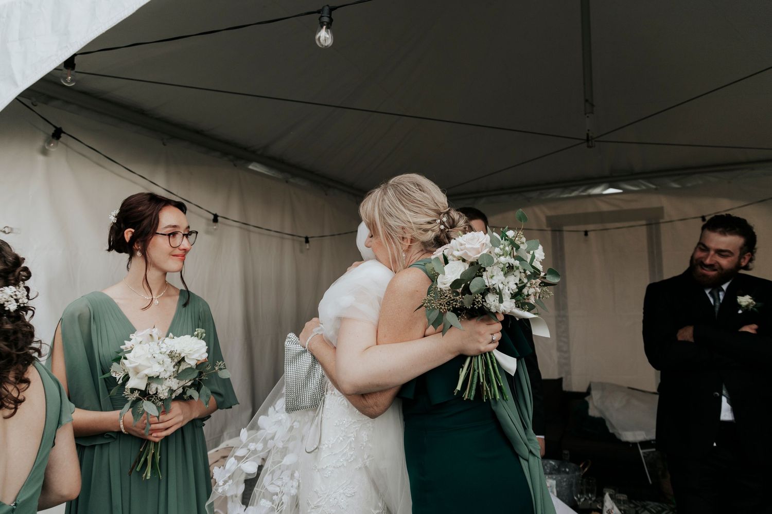 Wedding party in green dresses holding white bouquets during outdoor ceremony.