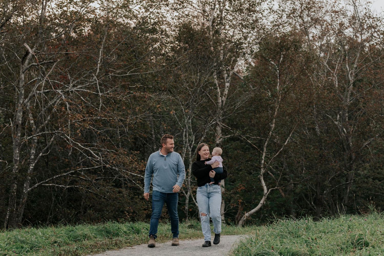 Family with baby strolling on path surrounded by autumn trees.