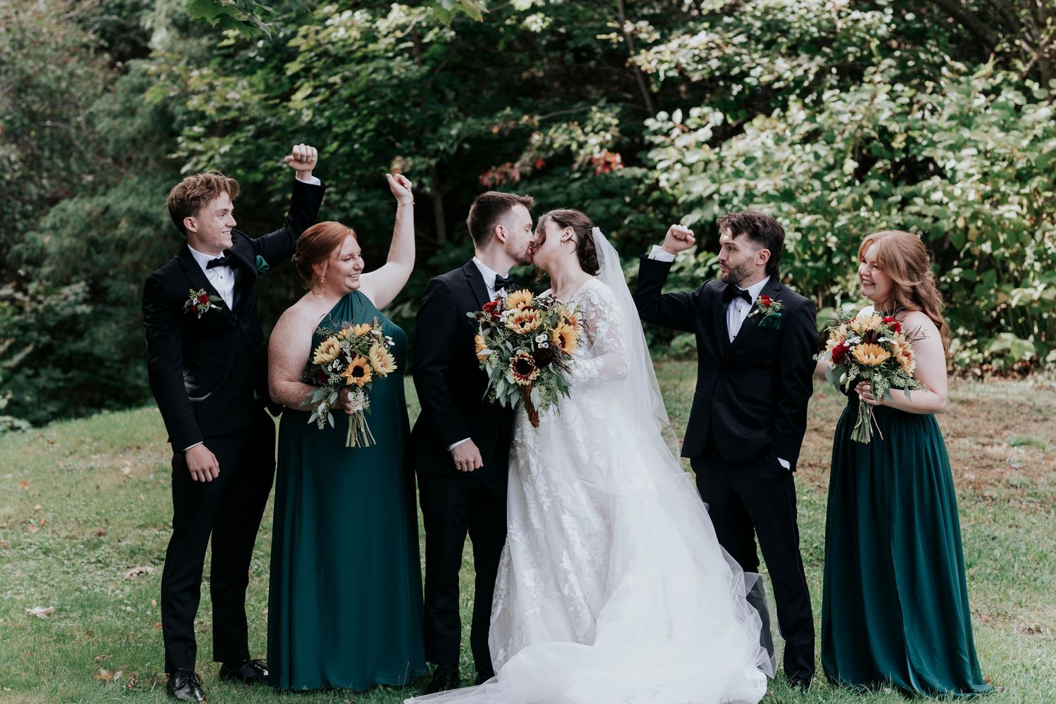 Wedding party in black suits and emerald green dresses celebrating outdoors.